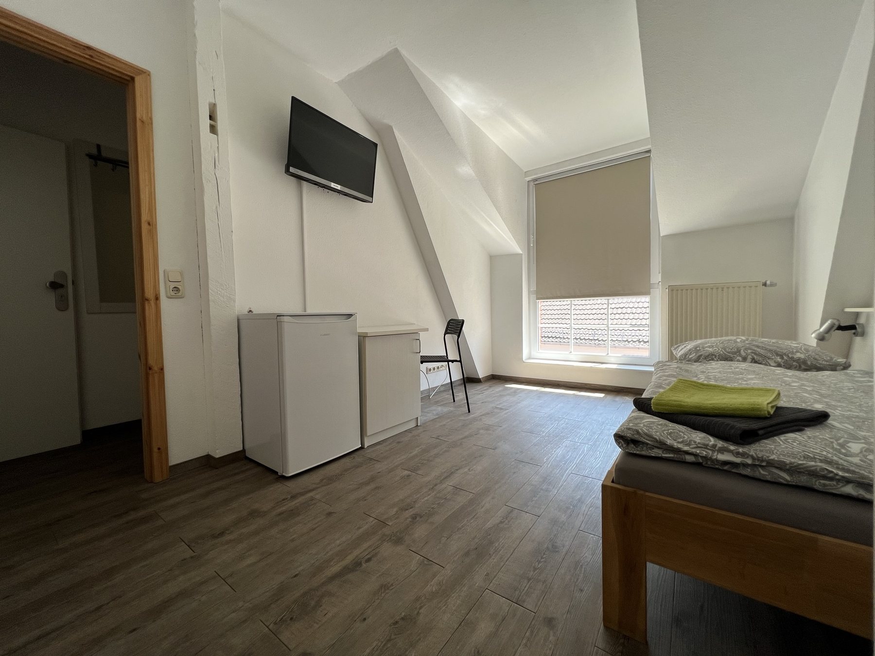Einzelzimmer mit Bett, Fernseher, Kühlschrank und Arbeitsplatz