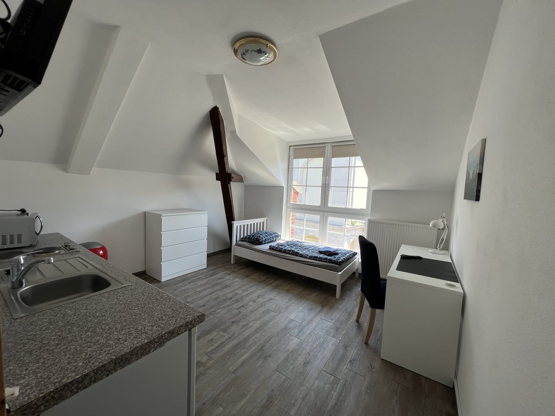 Einzelzimmer mit Bett, Arbeitsplatz und kleiner Küchenzeile